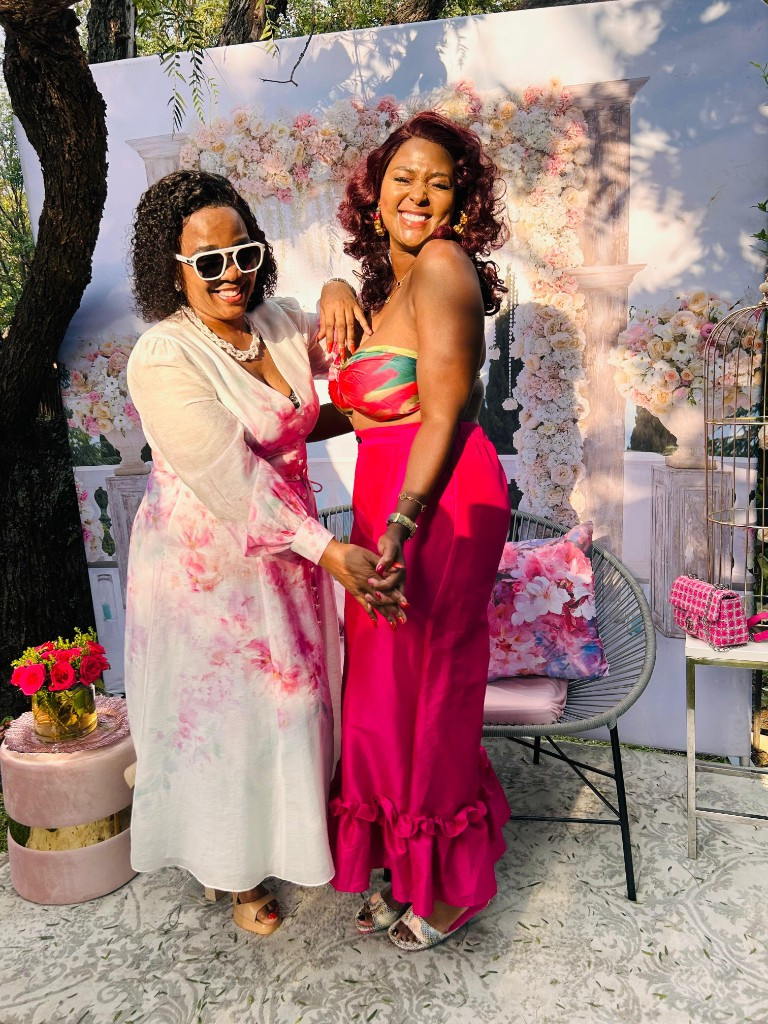 Two guests laughing at an outdoor celebration with floral backdrop